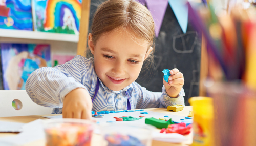 Portrait of smiling little girl working with plasticine in art and craft class of development school